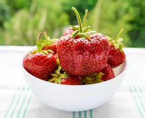 Fresh strawberries in a white bowl on a background of nature. Close-up.