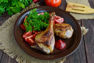 Roasted goose leg, sauce, herbs and tomatoes in a clay bowl on wooden background