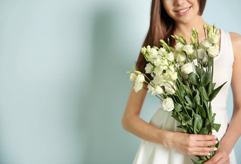 Beautiful young woman holding bouquet of white flowers on light background