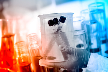 Gloved hand hold a beaker in laboratory room.