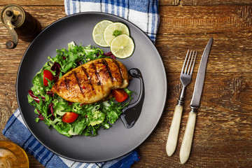 Grilled chicken breast with green salad on a black plate.