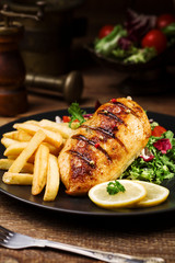 grilled chicken breast with green salad and french fries.