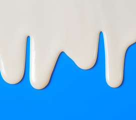 Dripping white milk, cream, paint yogurt on blue background