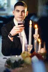 Close-up portrait of handsome groom, sitting by a table with decor and candles