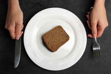 a slice of bread in a plate on a black background with Cutlery in the hands of women.The concept of poverty
