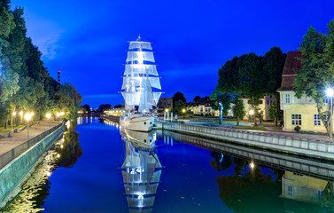 Beautiful sail yacht is docked on the Danes river. Night scene of Klaipeda old town district....