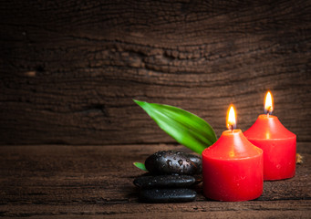 Red candle and black stones on wood background