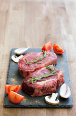 Raw beef steaks with ingredients on a black stone top view