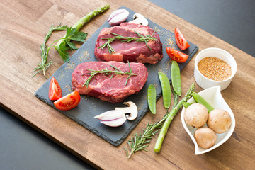 Raw beef steaks with ingredients on a black stone top view