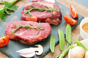 Raw beef steaks with ingredients on a black stone top view