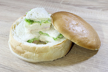 Sandwich box with chicken burger, tomatoes, ham, tuna, cheese on wood table.