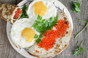 Scrambled eggs and pancakes with red caviar