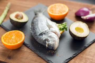 Roasted dorado or sea bream fish with vegetables, herbs and spices on silver tray over rustic wood backdrop, top view, copy space