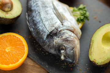 two raw dorado fish with lemon, spices and spoon on paper, composing on white wooden background, top view