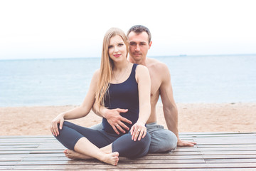 Fototapeta na wymiar Man and pregnant woman are doing yoga on the beach