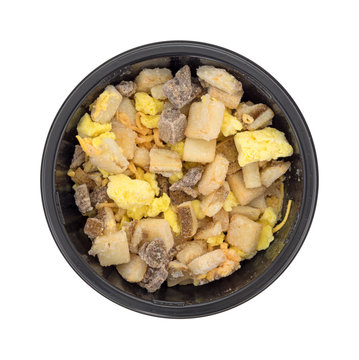 Frozen potatoes eggs and steak with cheddar cheese breakfast top view in a black tray isolated on a white background.