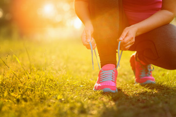 Woman lacing running shoes before workout. Lens flare.