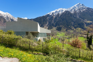 Fototapeta na wymiar Mountain house in cement, outdoors. The sky is blue and the house has a huge garden. Snow can be seen on the mountains in the background