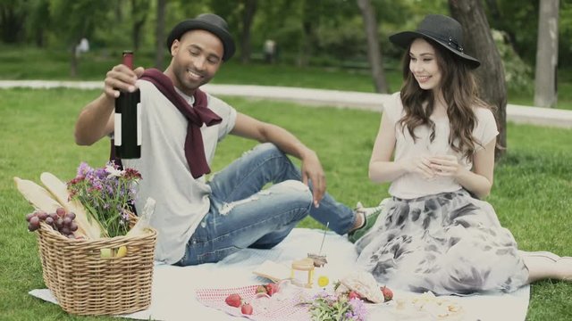 Smiling young couple having picnic and drinking wine outdoors