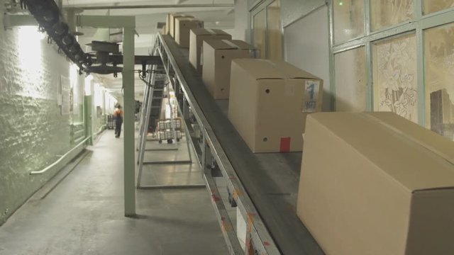 Moving conveyor belt with cardboard boxes along corridor in workplace.