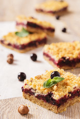 Honeysuckle crumb cake cut into square pieces on a light wooden background with berries and nuts 