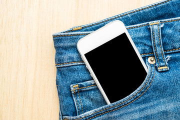 Mobile phone in blue jeans trousers on wood background