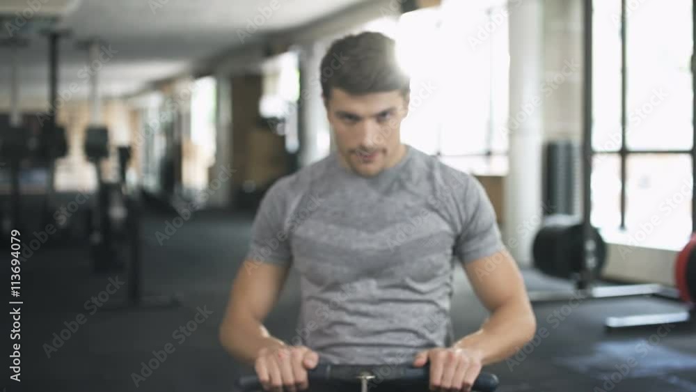 Poster handsome concentrated man doing exercise on fitness machine in gym