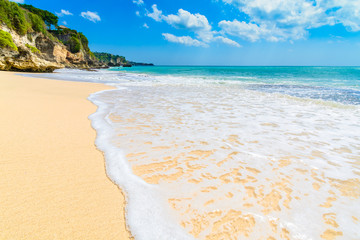 Waves washing up over a sandy beach in Bali with a rocky headland and horizon in the distance