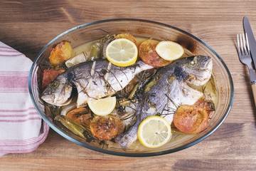 Baked fish with carrot,lemon and greenery.From above