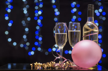 Background image with blue bokeh, a bottle of wine with two glasses, balloons and streamers. Gold and pink colour scheme. Taken with copy space.