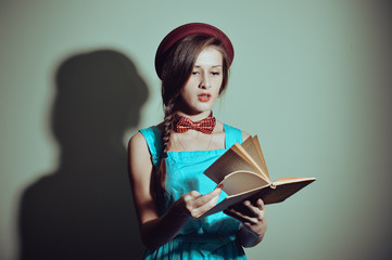 Beautiful female reading a book against light wall background, 