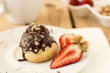 Small homemade profiterole with chocolate topping on wooden background 