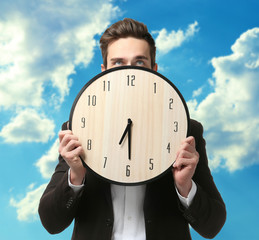 Man in black suit holding big clock on sky background