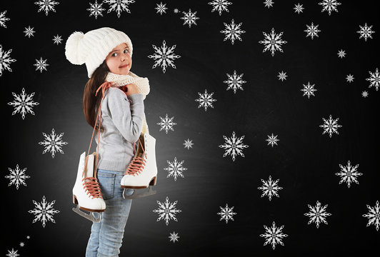 Little girl with skates in trendy knitted clothes and drawn snowflakes on blackboard background