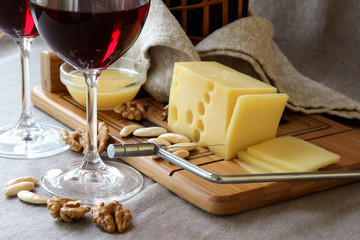 Piece of cheese on a board, wine glasses and nuts..