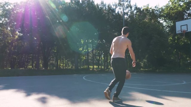 Young muscular man playing basketball in the park