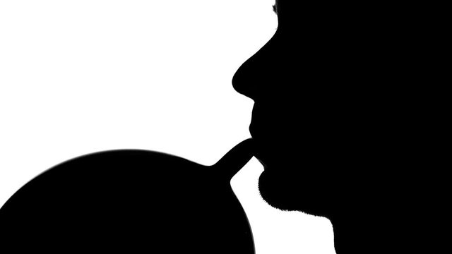 Man takes to his mouth a balloon and inflates it. Silhouette. Close up. White