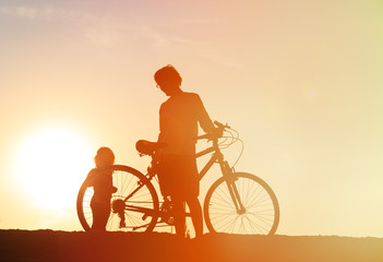 Obraz na płótnie Canvas Silhouette of father and little daughter biking at sunset