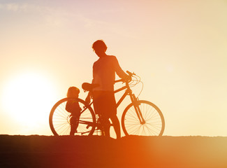 Fototapeta na wymiar Silhouette of father and little daughter biking at sunset