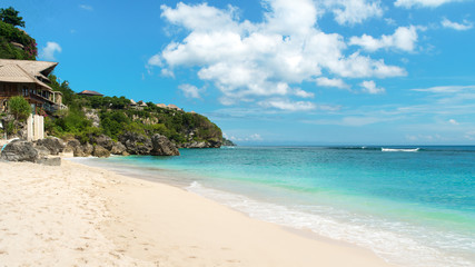 Beautiful tropical beach at midday with small waves breaking on the shoreline and a rocky headland in the distance.
