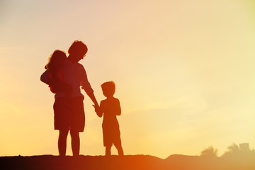 Fototapeta na wymiar father and two kids walking on beach at sunset