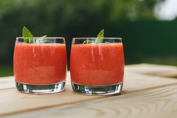 glass of strawberry smoothie on wooden table with mint