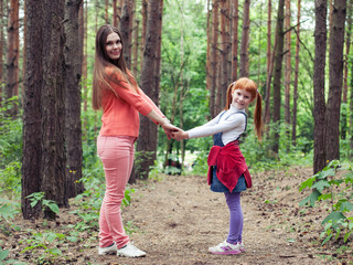 Mother and daughter holding hands and smiling in the woods