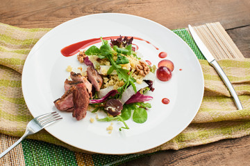 A healthy Breakfast consisting of a salad with duck breast, daikon, grapes and couscous served on a white plate