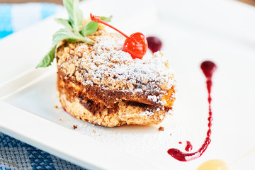 A sweet dessert consisting of crumble with applesauce and cherry topping served on a white plate