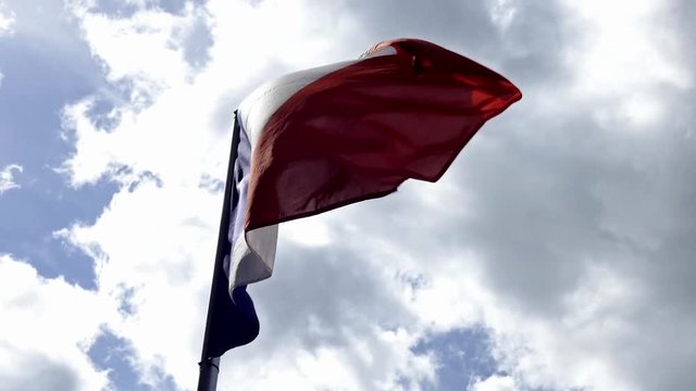 National flag of France waving in the wind in a sunny day with a cloudy sky in background