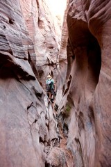 Man hiker squeezing through Zebra slot canyon, Escalante National Monument, Utah, USA. 