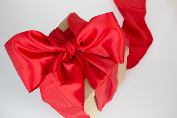 Brown gift box wrapped in wide red satin ribbon with a bow.