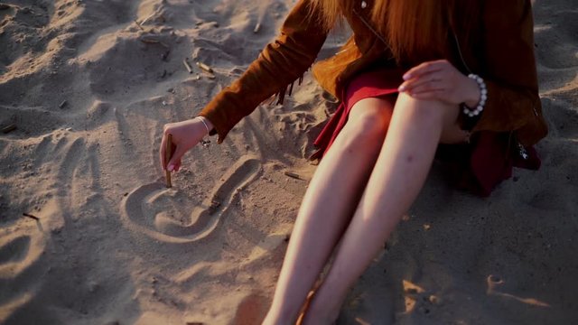 beauty girl draws a heart on the sand on sunset beach