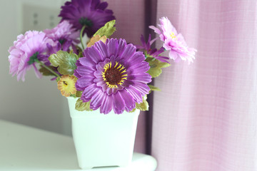 Purple flowers artificial in a white vase.
